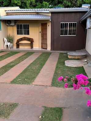 A house with a paved driveway, a bench, and a small garden with pink flowers. - Casa Flor do Ipê Homes (Nobres)