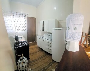 A compact kitchen with a gas stove, a microwave, and a refrigerator. There is a small table with a decorative item and a chair. - Casa Flor do Ipê Homes (Nobres)