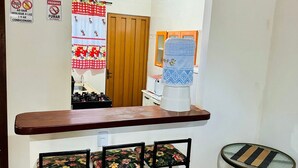 A small kitchen area with a wooden counter, a coffee machine, and two bar stools. There are two signs on the wall, one warning against smoking and the other advising to turn off the lights when not in use. - Casa Flor do Ipê Homes (Nobres)