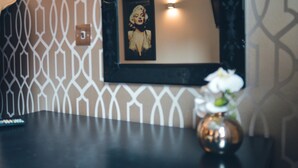 Une pièce avec un mur orné d’un motif, un tableau encadré, un vase de fleurs et une télécommande posée sur une table.