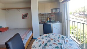 A compact room with a bed, a small kitchenette, and a balcony with a view. - Studio at the marinas (Saint-Cyprien)