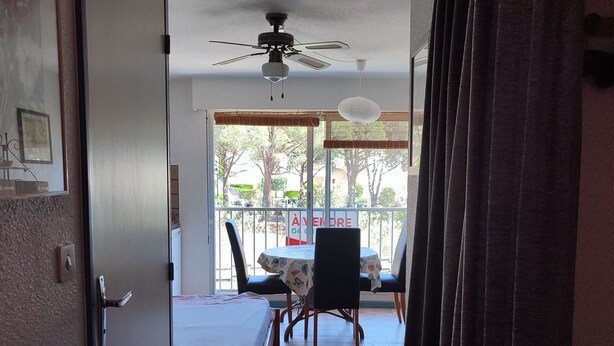 A hotel room with a bed, a small table, a ceiling fan, and a view of the outside through a window. - Studio at the marinas (Saint-Cyprien)