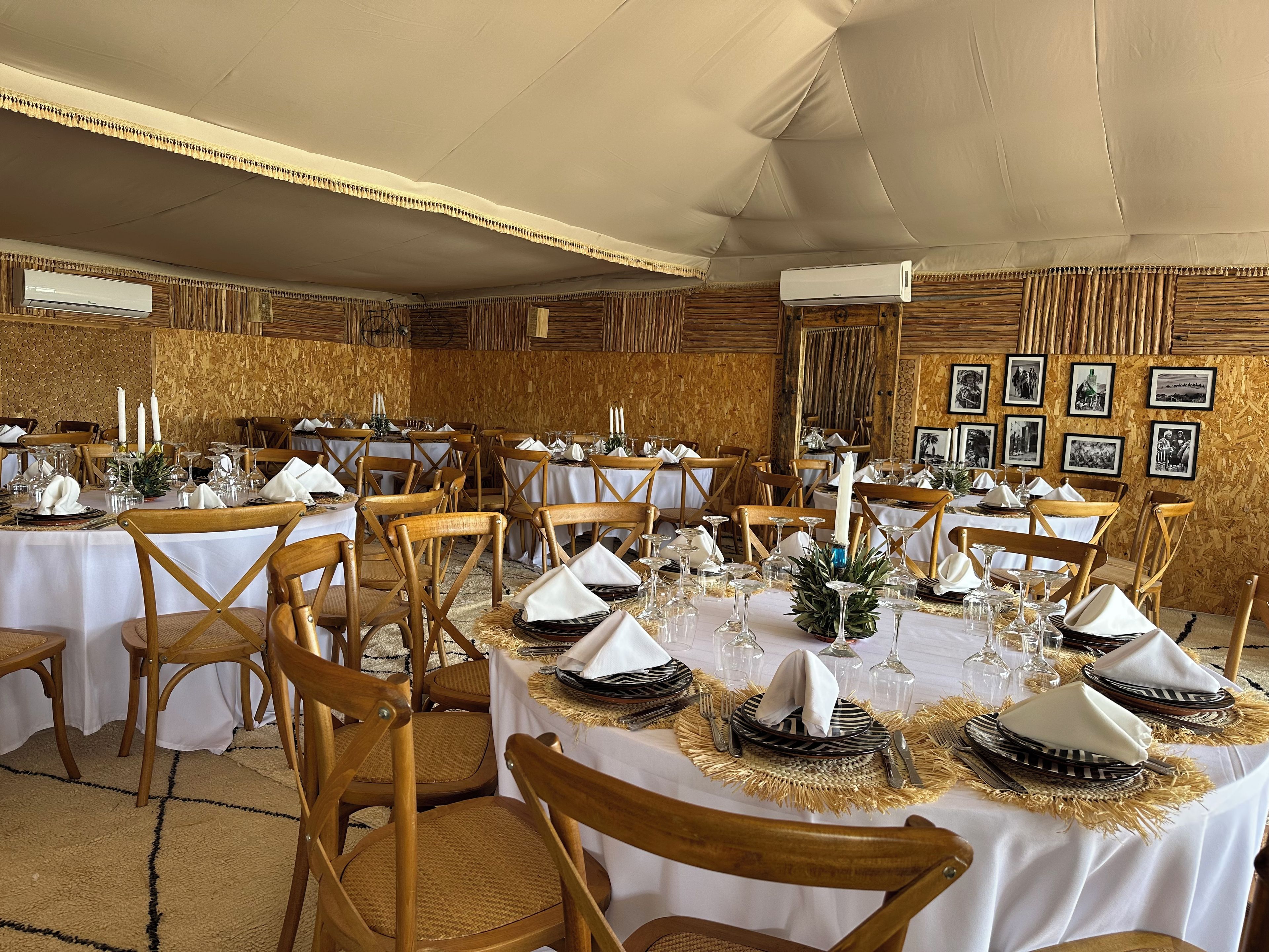 A banquet hall with round tables set for dining, wooden chairs, and a wall adorned with framed pictures.