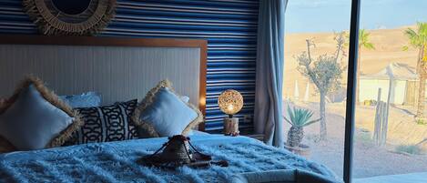 Un dormitorio con una cama grande, cabecera y vista al desierto a través de un ventanal.