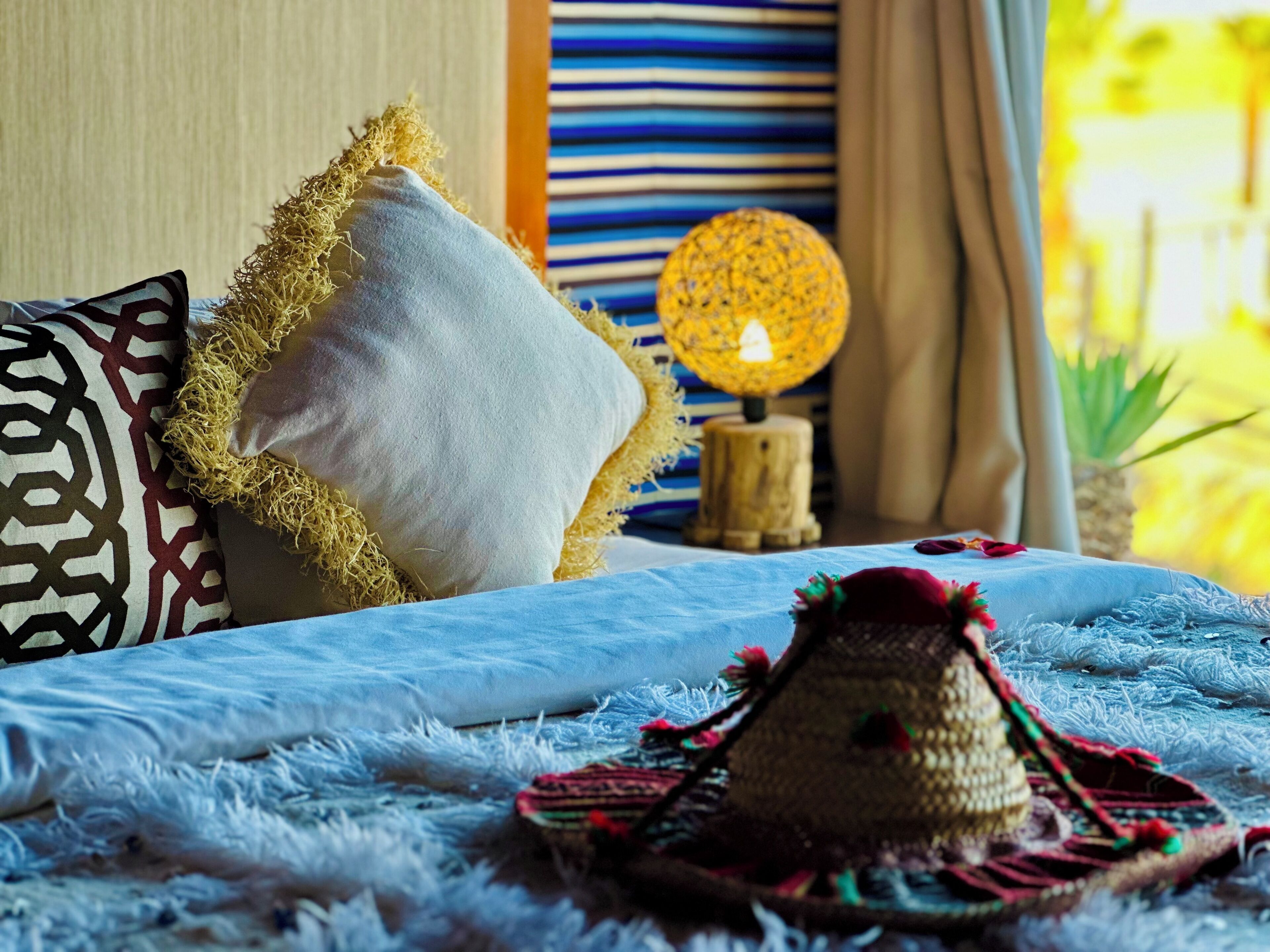 Una cama con una manta azul, un sombrero de paja y una almohada estampada.