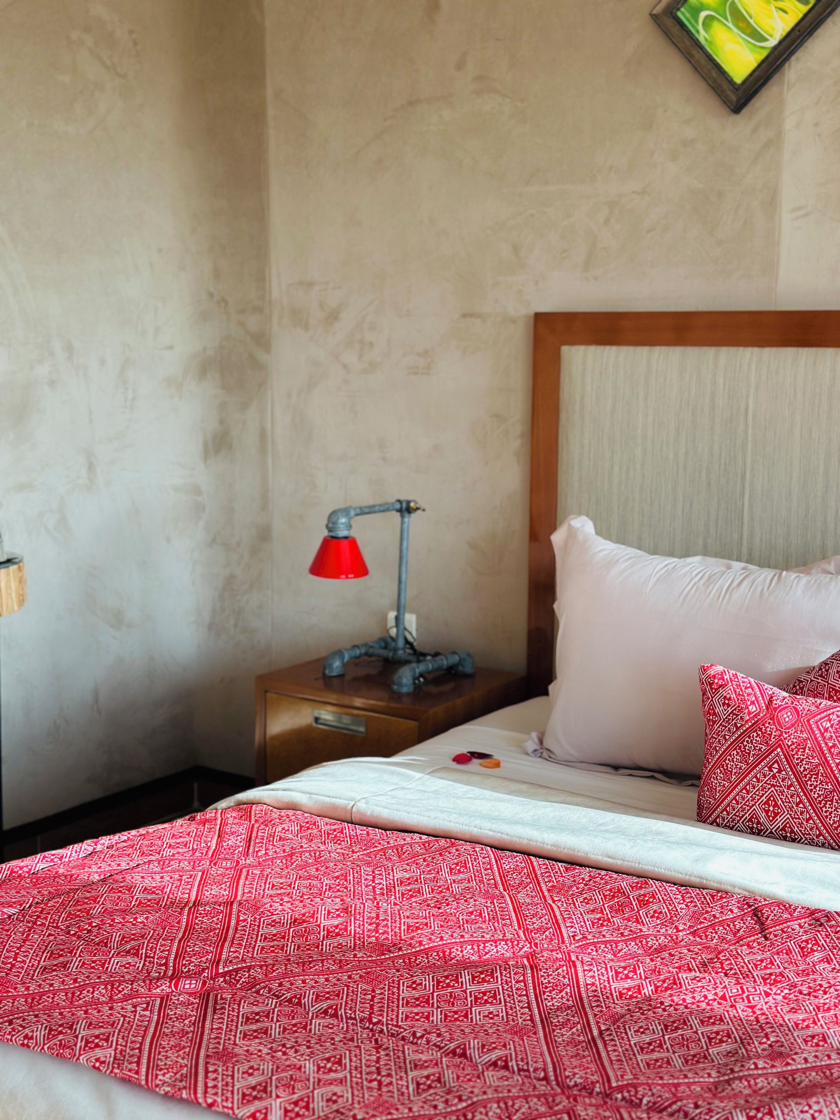 A bedroom with a bed, a nightstand, a red lamp, and a pillow with a geometric pattern.