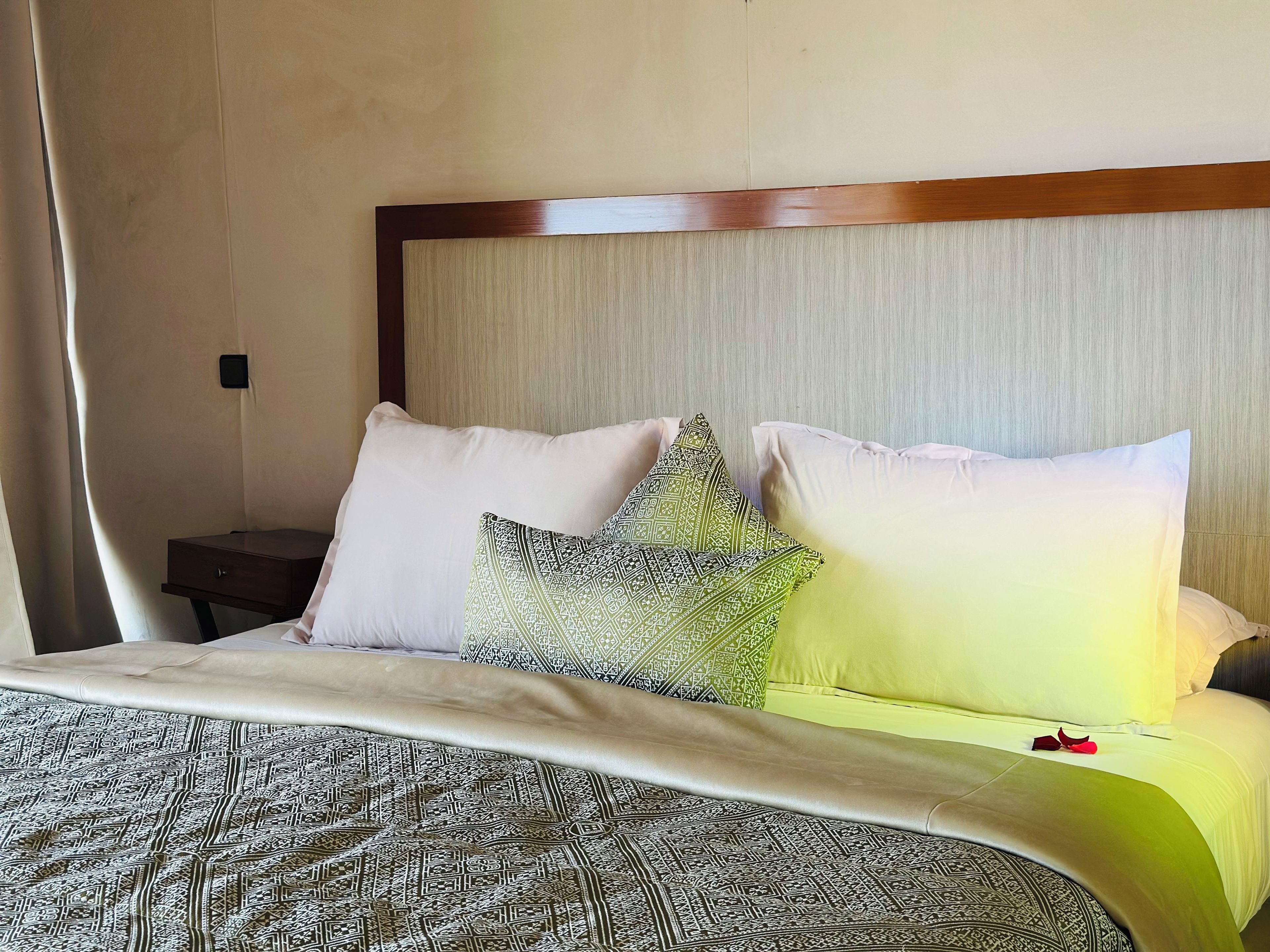 A neatly made bed with patterned bedding, a wooden headboard, and a bedside table with a lamp.