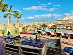 A poolside area with lounge chairs and a table, palm trees, and desert hills in the background. - Yes We Camps Luxury lodge & spa (Agafay)
