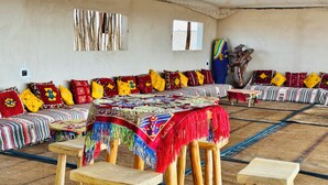 Ein Zimmer mit einer langen, gestreiften Sofaecke, einem Couchtisch mit bunter Decke und Holzschemeln.
