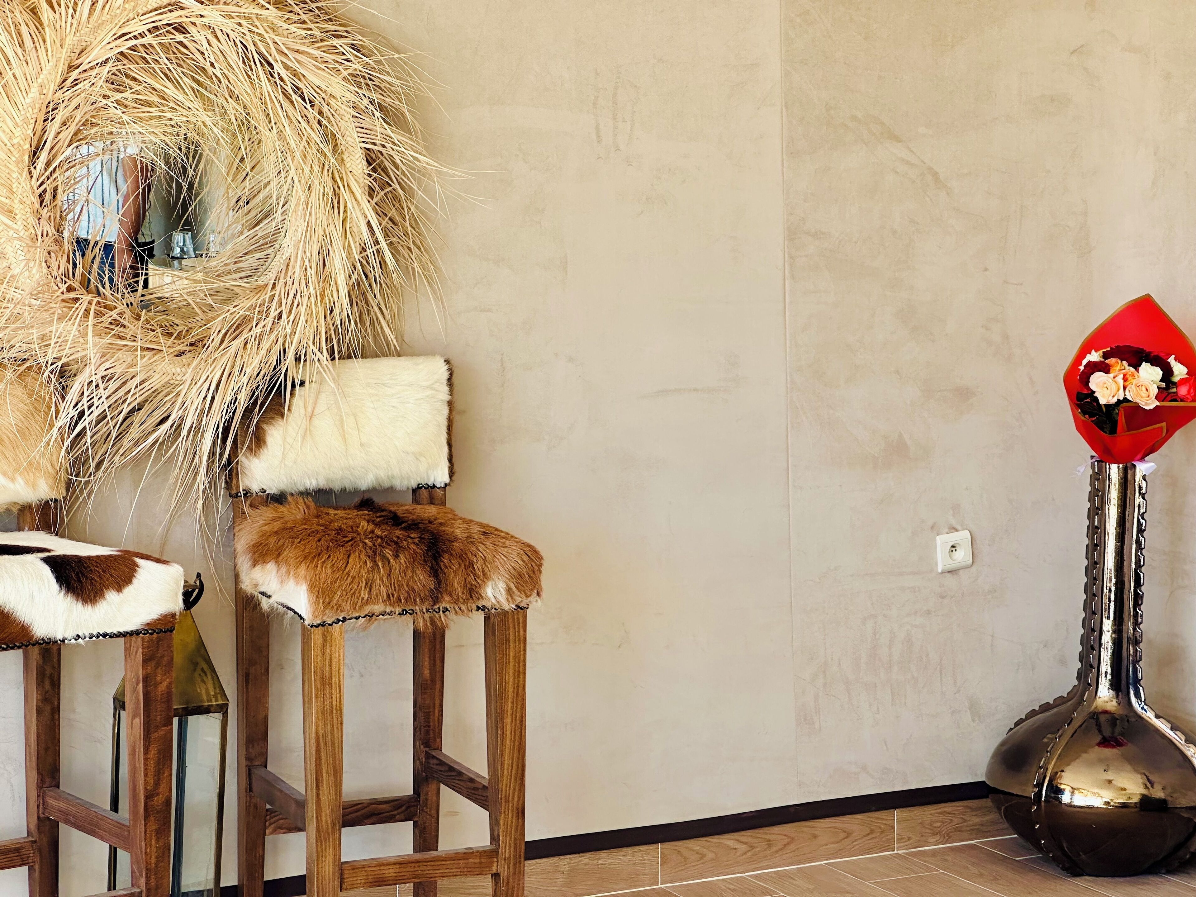 A room with a rustic chair, a decorative mirror, and a vase with flowers.