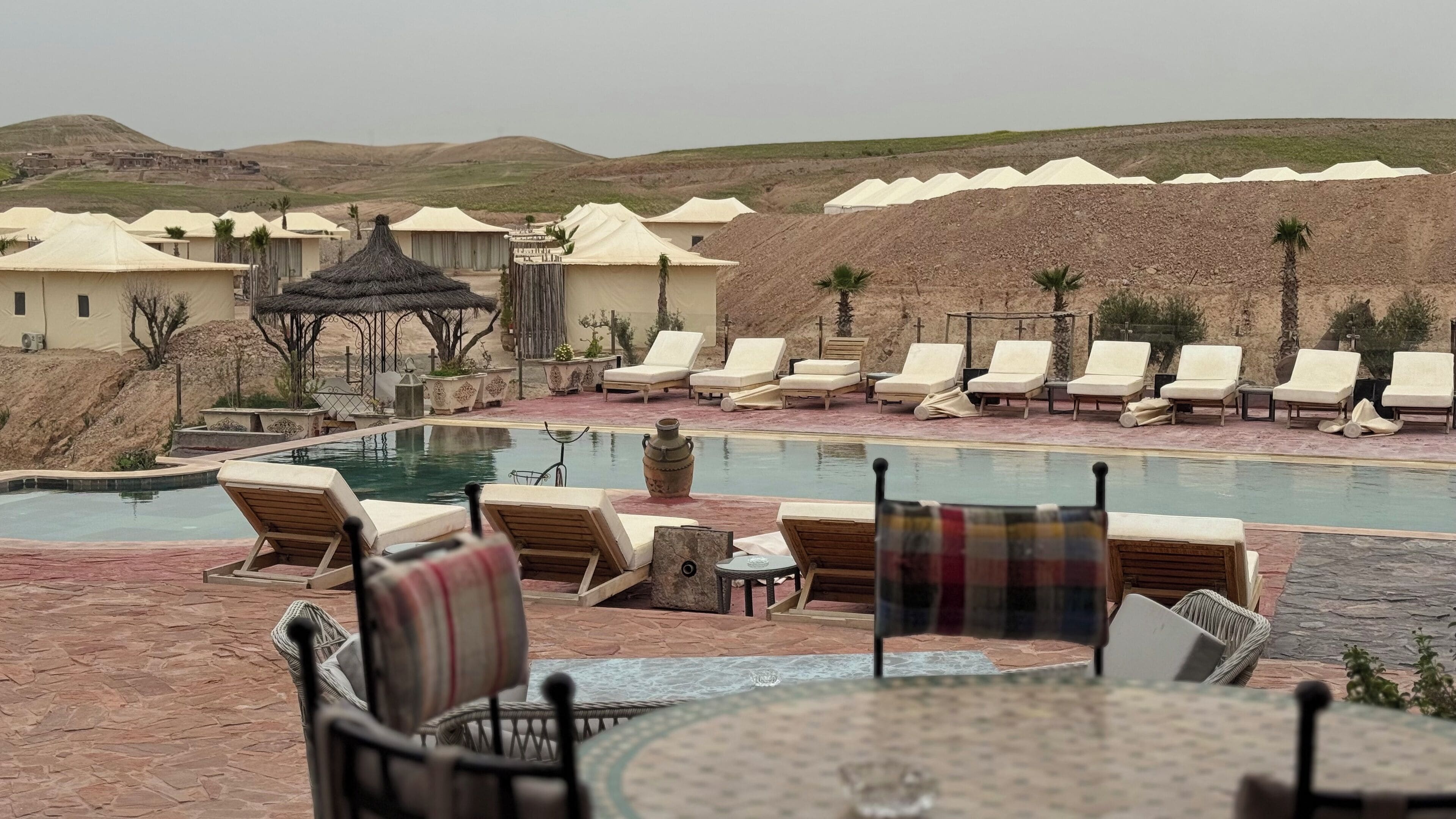 A poolside area with lounge chairs and umbrellas, surrounded by desert hills.