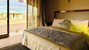 Ein Hotelzimmer mit Bett, Blick auf die Wüste und einer großen Schiebeglastür.