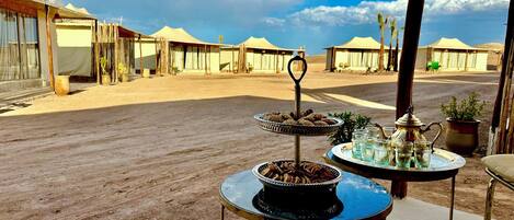 A desert setting with tents and a table with food and drinks.