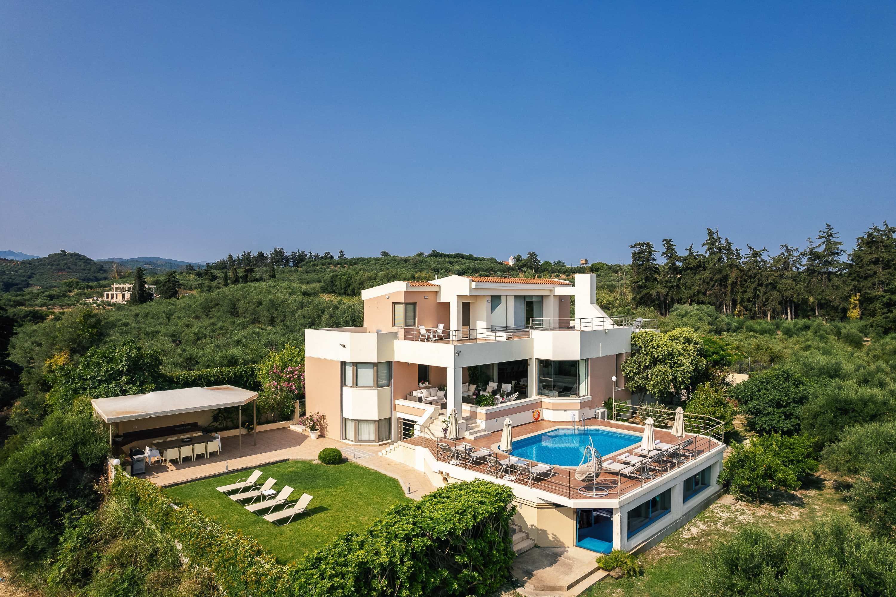 A modern two-story house with a swimming pool, surrounded by lush greenery and hills.