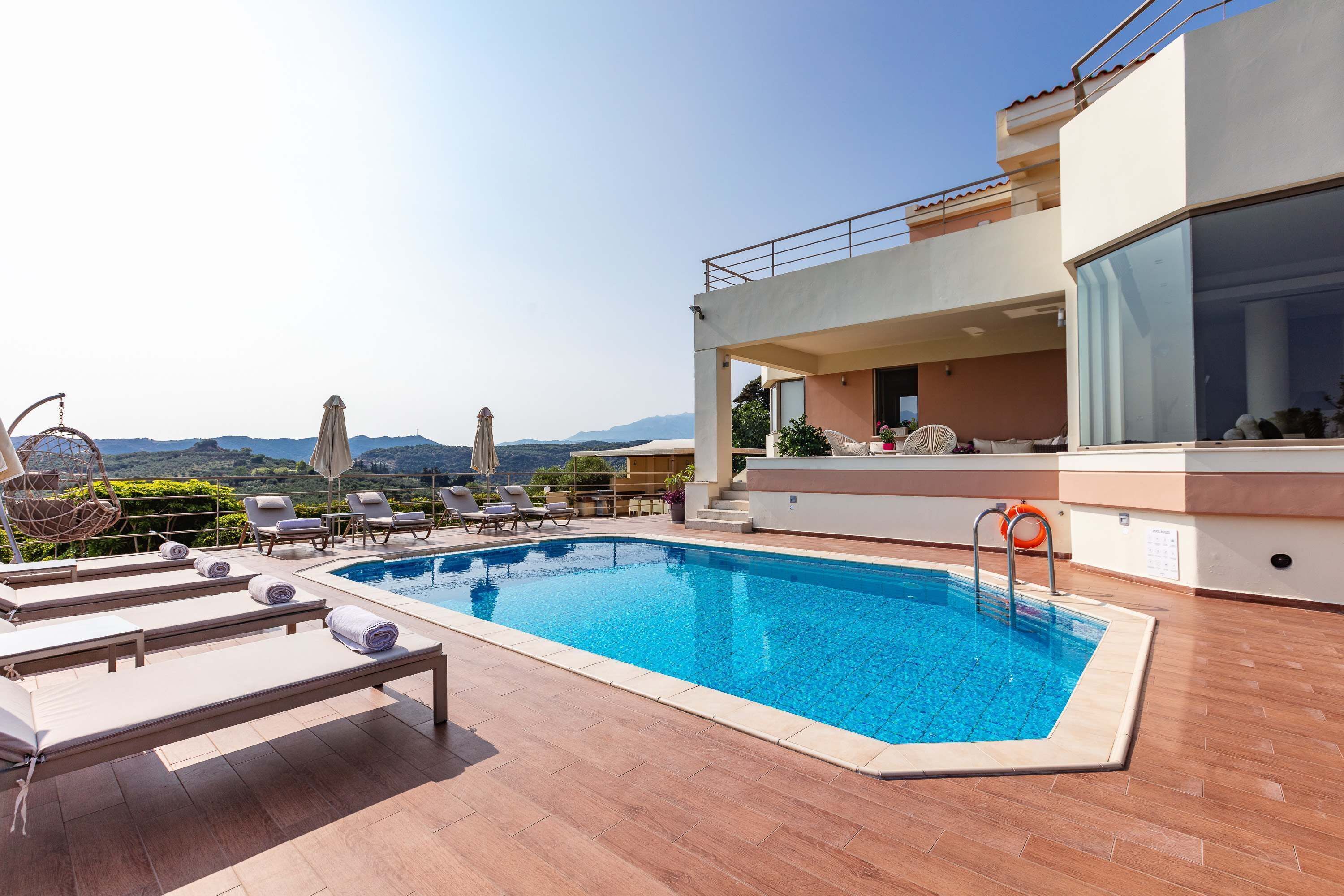 A rooftop pool area with lounge chairs, a swimming pool, and a view of the mountains.