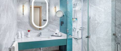 A modern bathroom with a marble wall, a teal vanity, a large mirror, and a glass-enclosed shower.