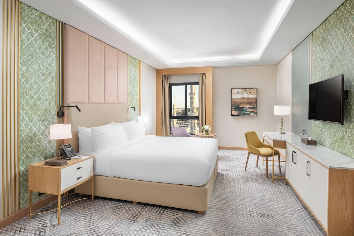 Een hotelkamer met een bed, nachtkastje, lamp, stoel, bureau en een televisie.