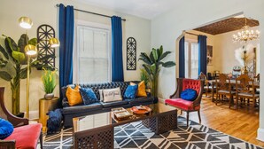 A living room with a black sofa, red chair, and a dining area with wooden chairs and a chandelier. - Happy Shack Ybor City-Historic District-Steps to 7th Ave (Tampa)