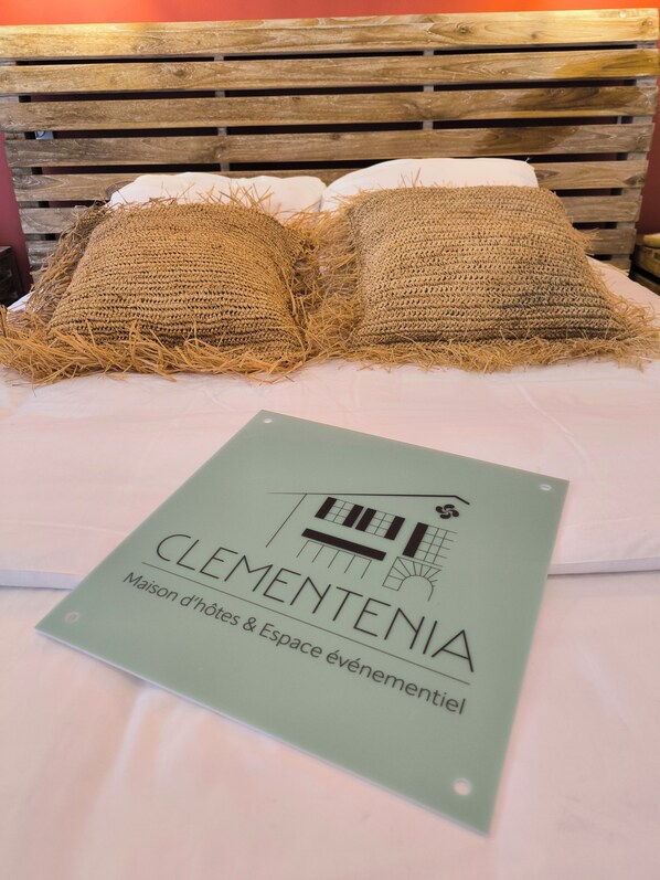 A bed with two textured pillows and a green sign on the bed. - Clementenia (Arneguy)
