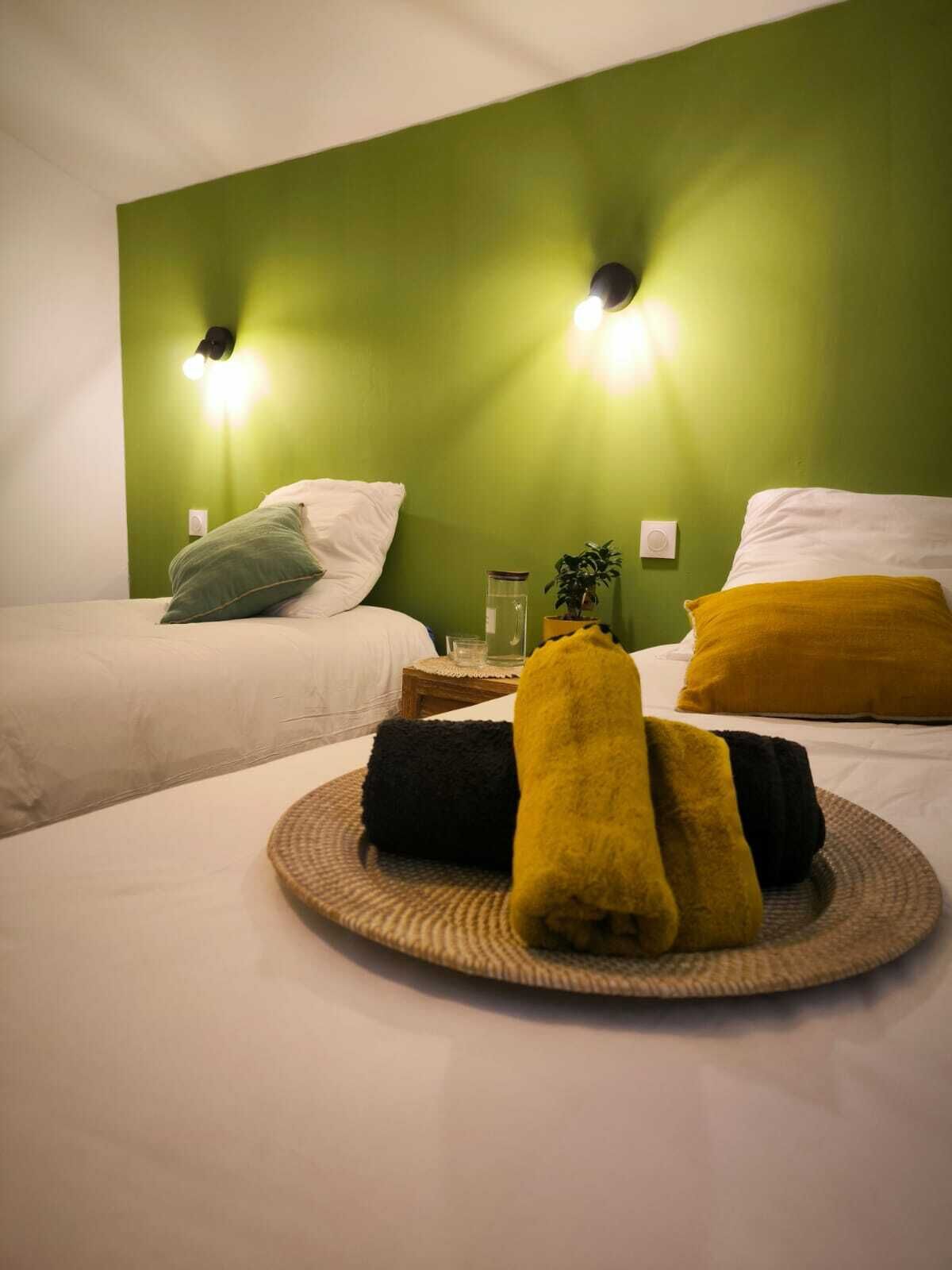 Une chambre d’hôtel avec deux lits, des murs verts et deux lampes fixées au mur.