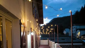 A corridor with a railing, string lights, and a view of buildings in the background. - Clementenia (Arneguy)