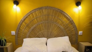 A bed with a woven headboard, two white pillows, and a basket with folded towels. - Clementenia (Arneguy)