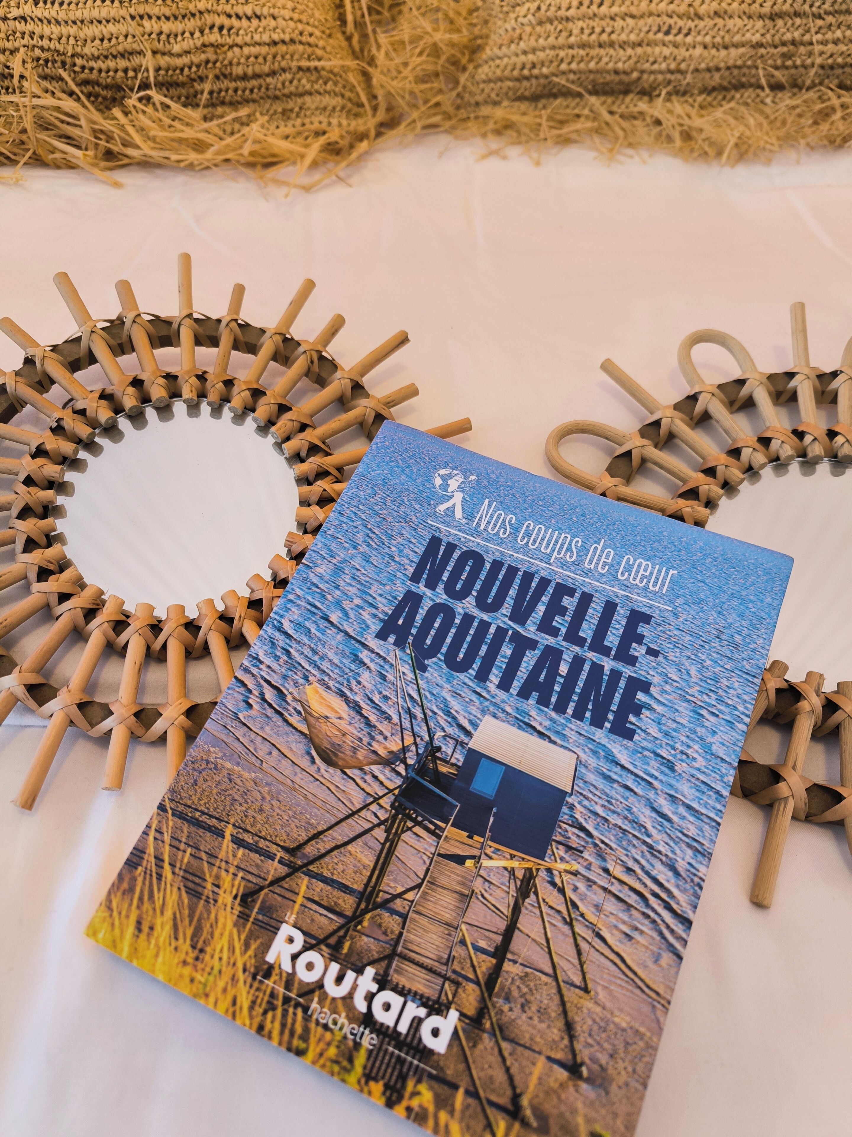 Un folleto con el título 'NOUVELLE AQUITAINE' muestra una escena de playa, colocado sobre una mesa con estructuras de madera trenzada.