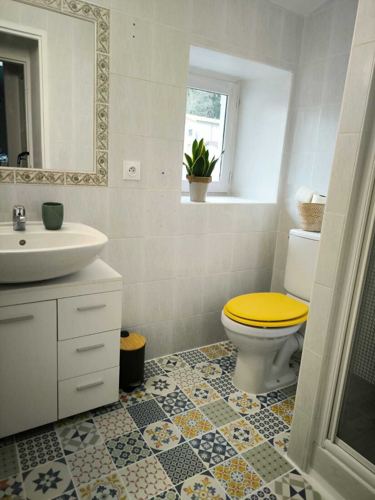 Un baño con lavamanos blanco, espejo, inodoro amarillo y ventana con planta.
