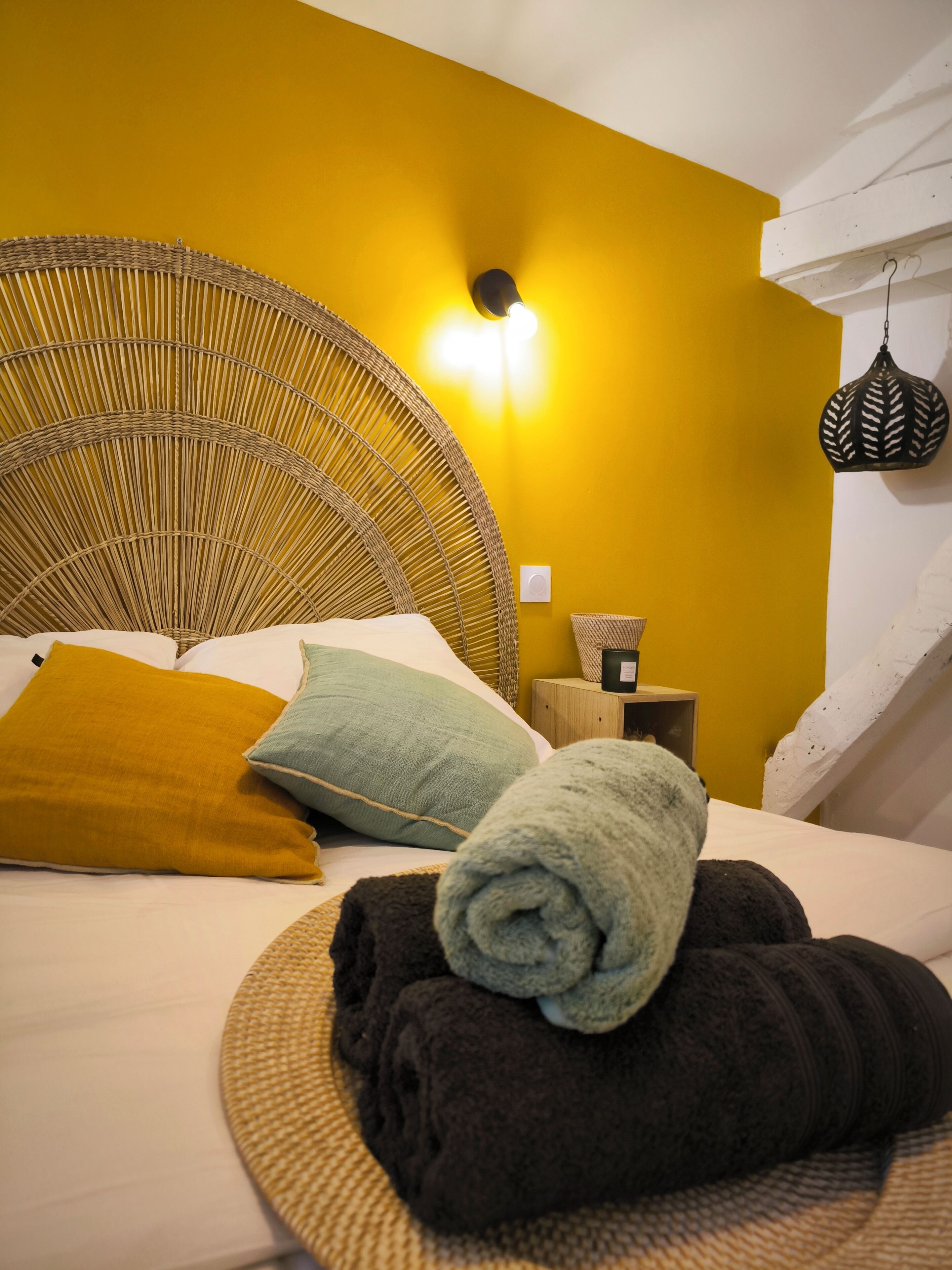 Una cama con cabecera trenzada, una mesita de noche con lámpara y una lámpara de pared.