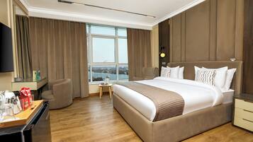 Una habitación de hotel moderna con una cama grande, un escritorio con una silla, una mesita con una lámpara y un ventanal con vistas a la ciudad.