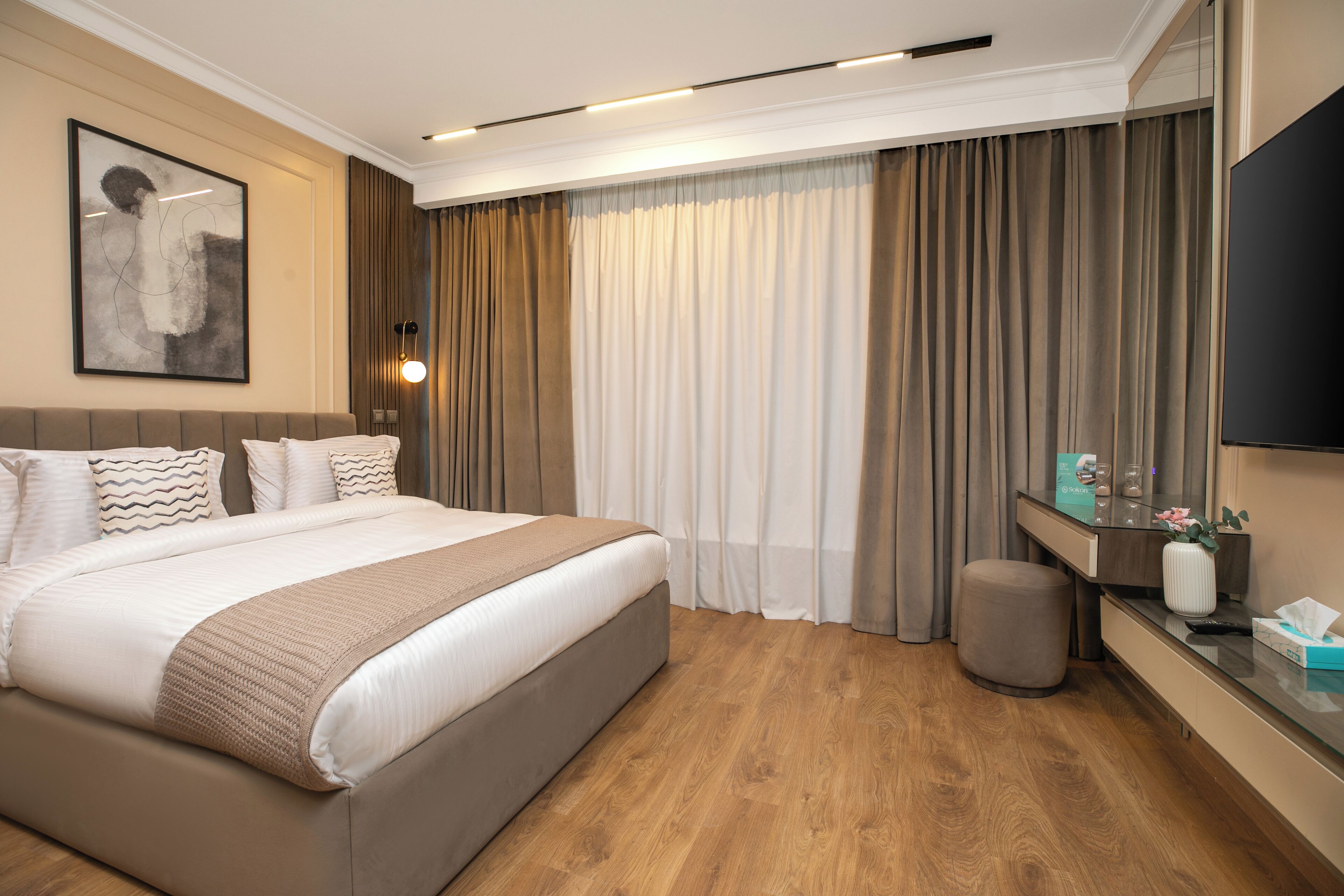 Une chambre d’hôtel avec un grand lit, un bureau avec un téléviseur à écran plat, une table de chevet et une grande fenêtre avec des rideaux.