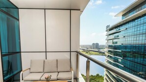 A balcony with a sofa and a table, overlooking a cityscape and a body of water. - Sokon Residence Nile View at Hilton (Cairo)
