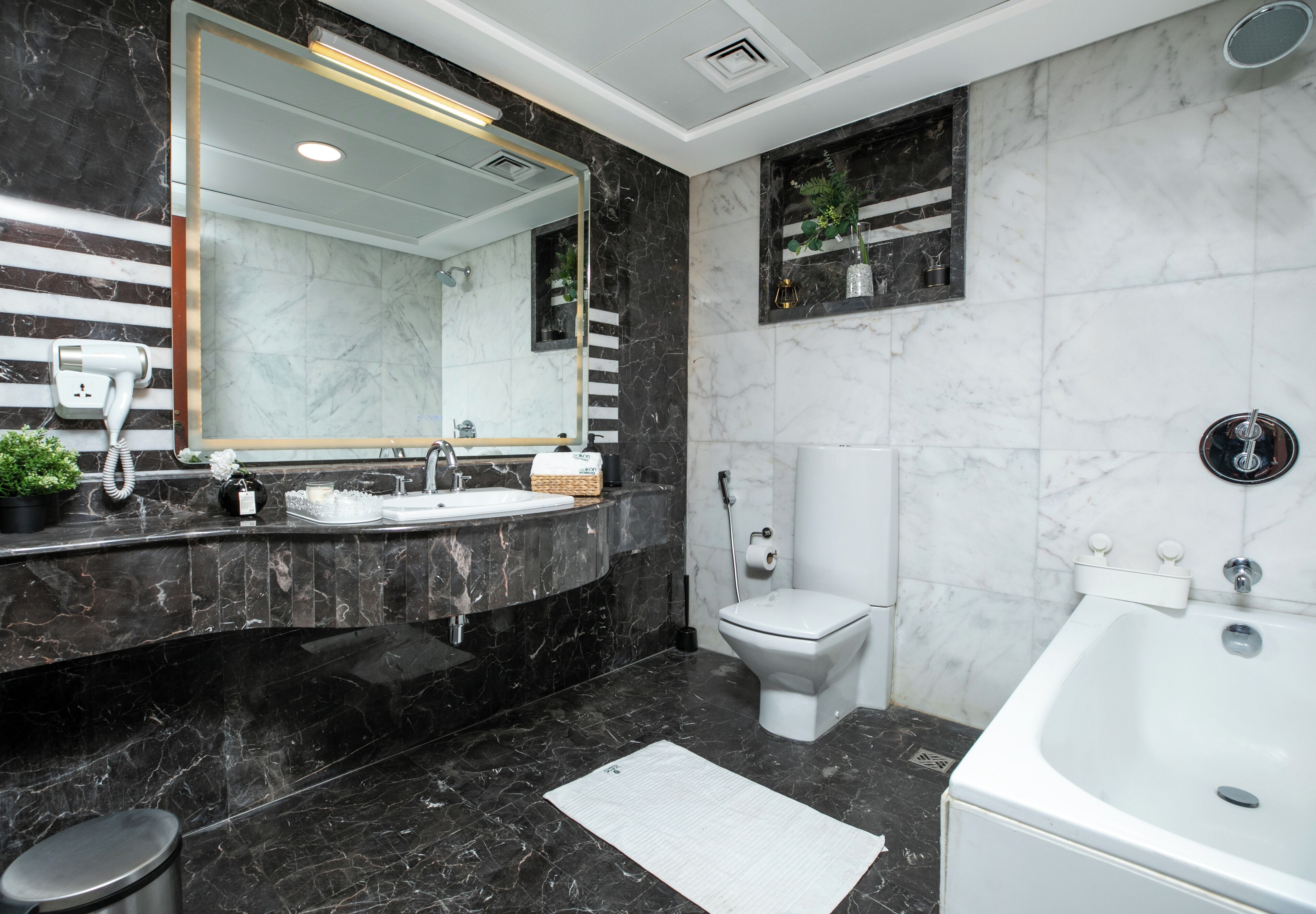 A modern bathroom with a large mirror, two sinks, a toilet, and a bathtub.