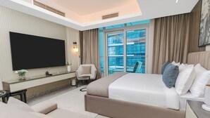 A modern hotel room with a large bed, a flat-screen TV, a seating area with a chair and table, and a view of the city through large windows. - Sokon Residence Nile View at Hilton (Cairo)