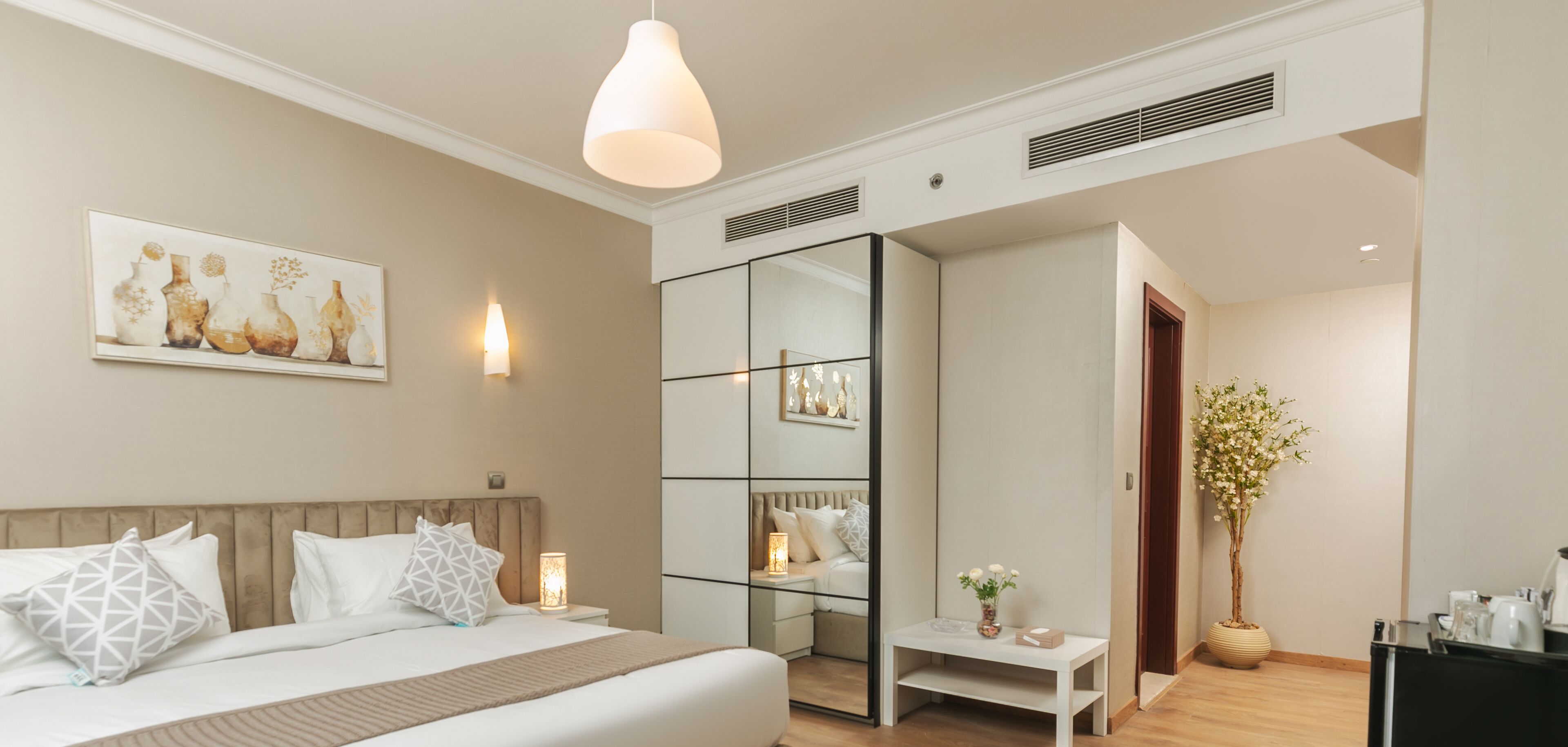 Un dormitorio moderno con cama, mesita de noche, lámpara y un espejo grande.