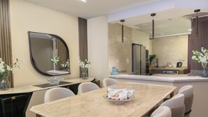 A modern dining area with a marble table, white chairs, and a large mirror. - Sokon Residence Nile View at Hilton (Cairo)