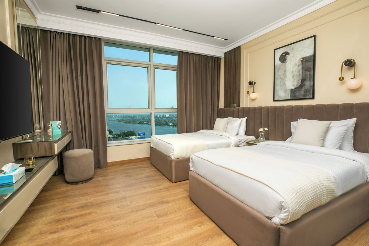 A hotel room with a large bed, a desk with a flat-screen TV, a window with a city view, and a painting on the wall.