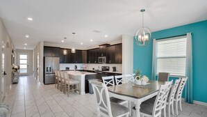 A modern kitchen with dark cabinets, a central island, and a dining area with white chairs.