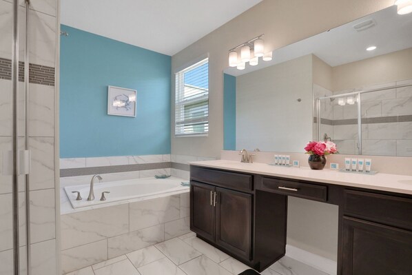 A modern bathroom with a bathtub, a large mirror, dark cabinets, and a blue accent wall. - 8966ccd-the Retreat At Championsgate 6 Bedroom Home (Davenport)