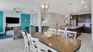 A modern kitchen with dark cabinets, a central island, and a dining area with a wooden table and white chairs.
