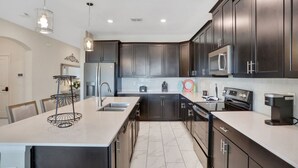 A modern kitchen with dark cabinetry, stainless steel appliances, and a central island with a light-colored countertop.