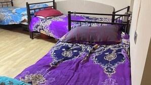 Ein Schlafsaalzimmer mit zwei Einzelbetten, jeweils mit einem gemusterten Bettbezug und Kissen. Der Raum hat einen Holzboden und weiße Wände.