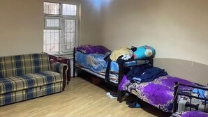 Ein kleiner, einfach eingerichteter Raum mit einem Karo-Sofa, einem Bett mit bunter Decke und einem Fenster mit Blick.