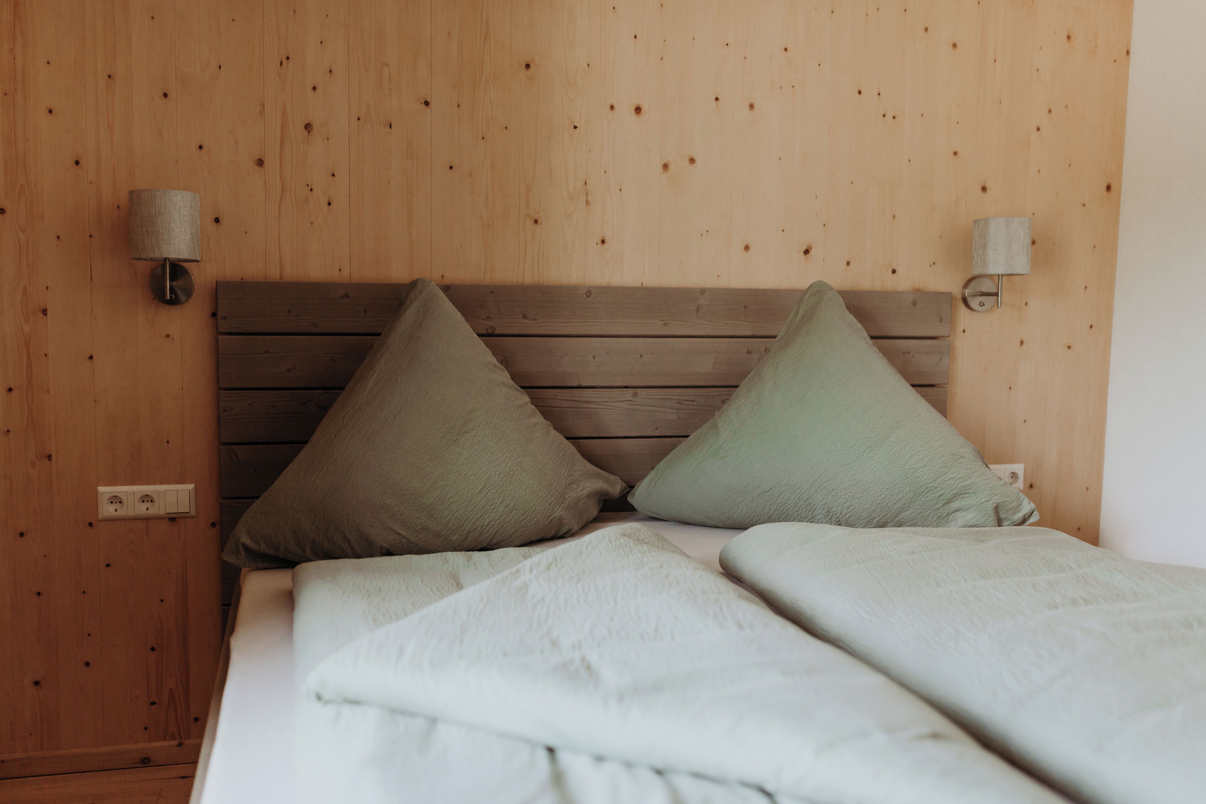 Ein Zimmer mit Holzwänden, einem Bett, zwei Kissen und Wandleuchten.
