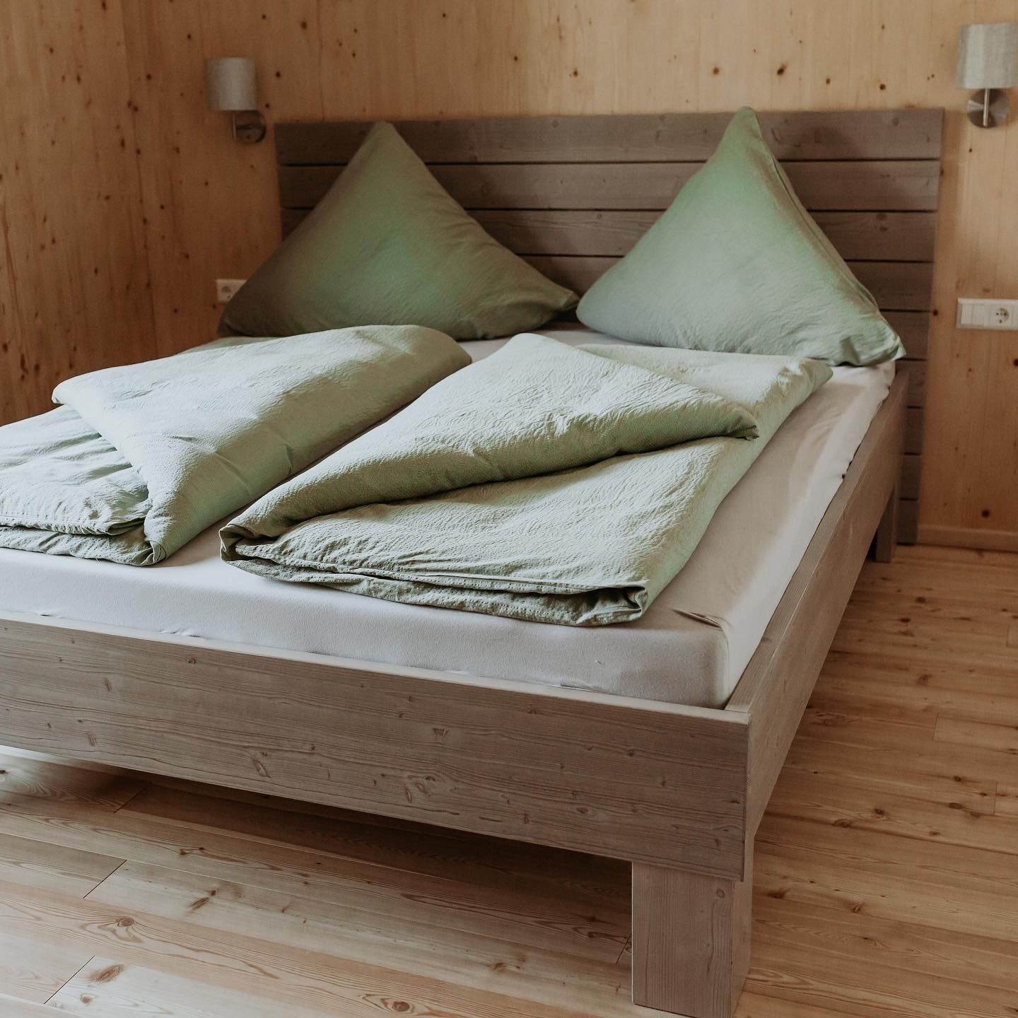 A wooden bed with a mattress and pillows, a nightstand with a lamp, and a wooden floor.