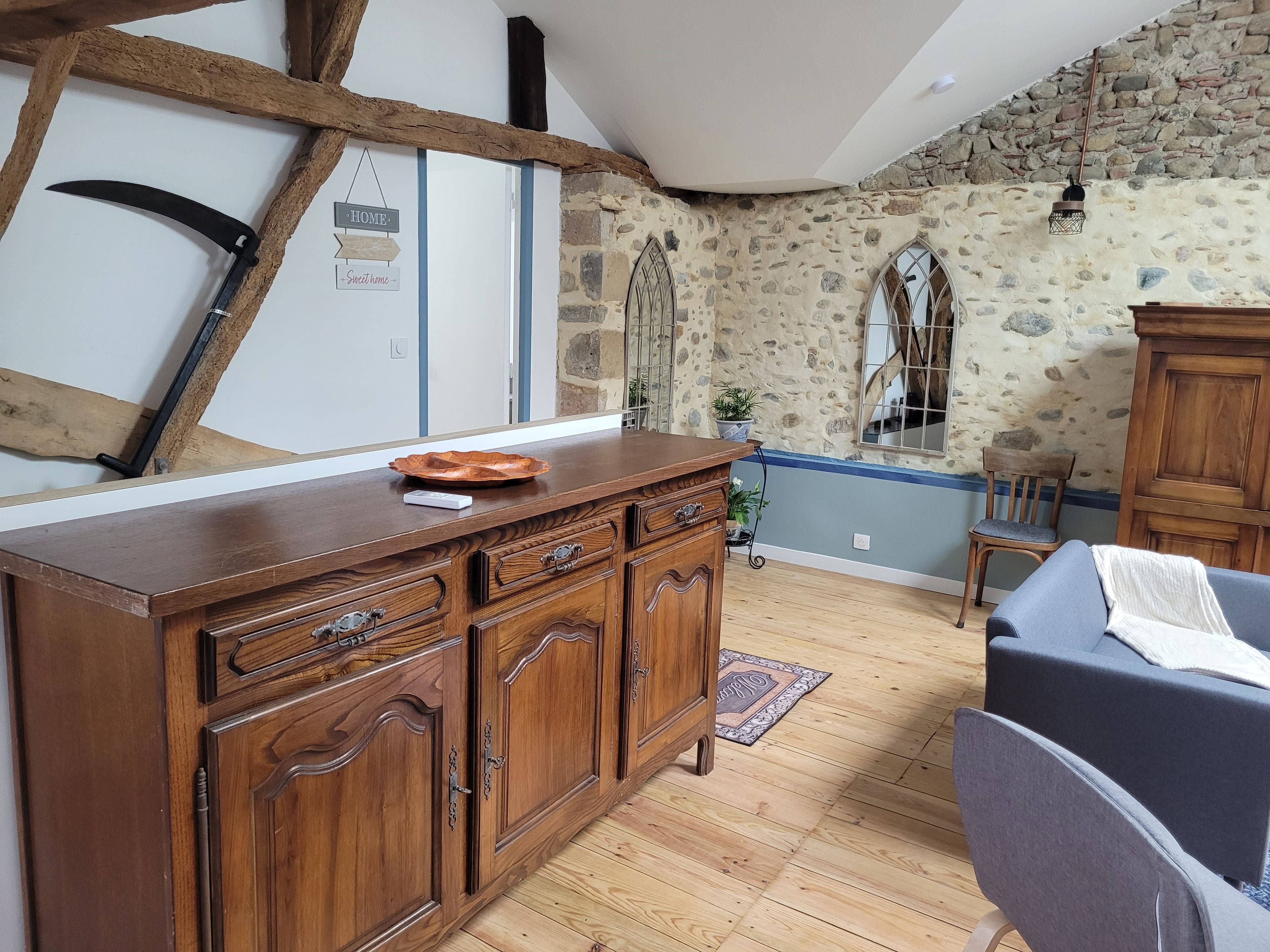 A rustic kitchen with wooden cabinets, a stone wall, and a blue ceiling.