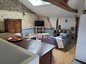 A cozy living space with a kitchen area, a television mounted on the wall, and a wooden ceiling.