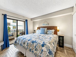 A bedroom with a bed, a 'RELAX' sign, a nightstand, and a view of the outside balcony.