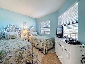 A bedroom with two beds, a TV, and a dresser. - Gulfside Retreat | Sunrise & Sunset (St. Pete Beach)