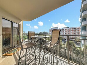 A balcony with a table and chairs, overlooking a cityscape with buildings and a clear sky. - Gulfside Retreat | Sunrise & Sunset (St. Pete Beach)